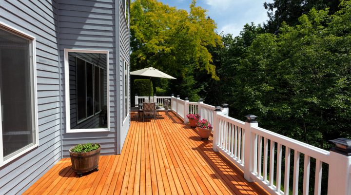 A bright and sunny wooden deck with ample seating and lush greenery in the background, ideal for relaxation and outdoor entertainment.