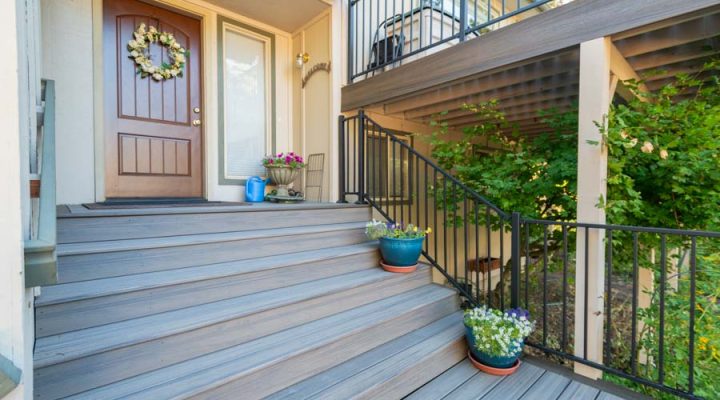 A welcoming home entrance featuring a gray deck with colorful potted plants and a wreath on the door, showcasing a friendly and decorative approach.