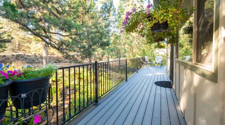 Long view of a residential deck surrounded by mature trees, with vibrant hanging and potted flowers, providing a serene outdoor living space.