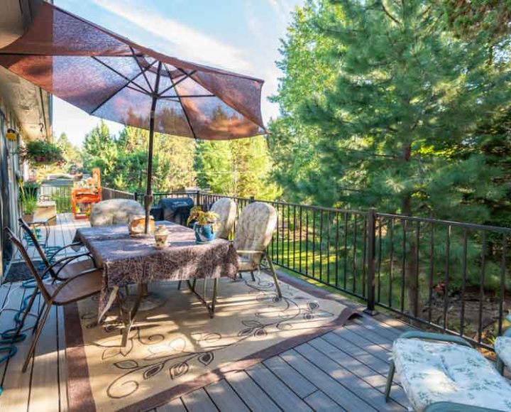 A charming deck dining area under a large umbrella, with comfortable seating and lush greenery surrounding, perfect for outdoor meals or gatherings.