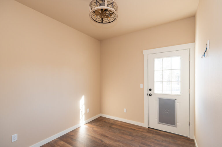 Bright entry space with beige painted walls, dark wood laminate flooring, white door with built-in pet door, and decorative ceiling fixture—welcoming and practical for ADU living.