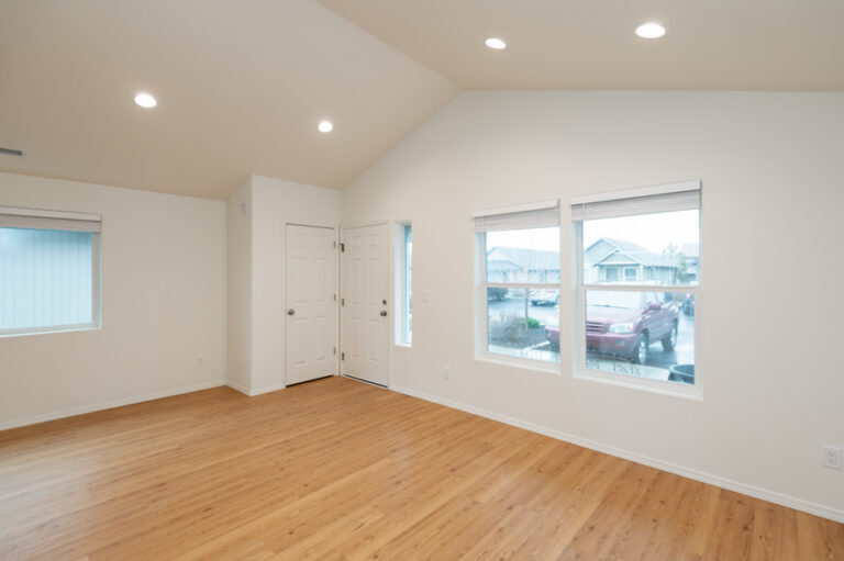 Spacious, move-in-ready living area with white walls, recessed lighting, light wood floors, and large windows offering natural light and neighborhood views.